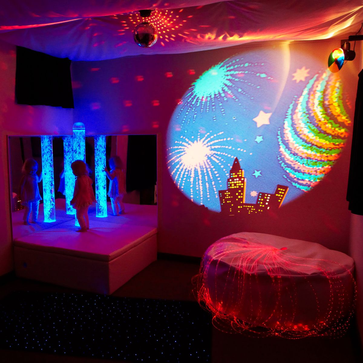 Calming Sensory Room Package with Kid standing on platform next to blue bubble tube with red fiber optic lights and projector slide