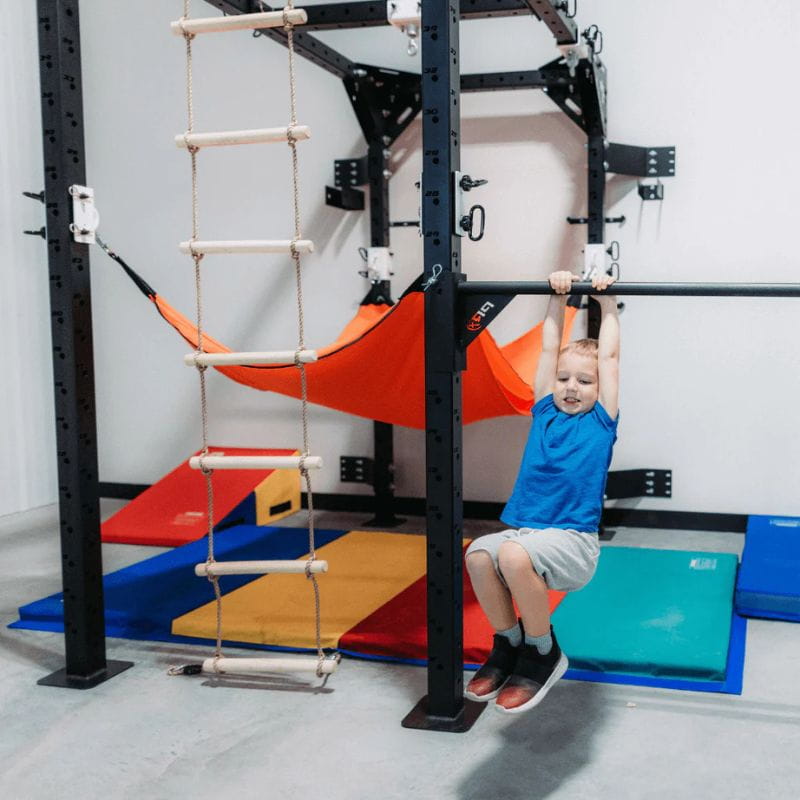 Child swinging from bar on the Sensory RX Commercial Space-Saving Sensory System along with other attachments