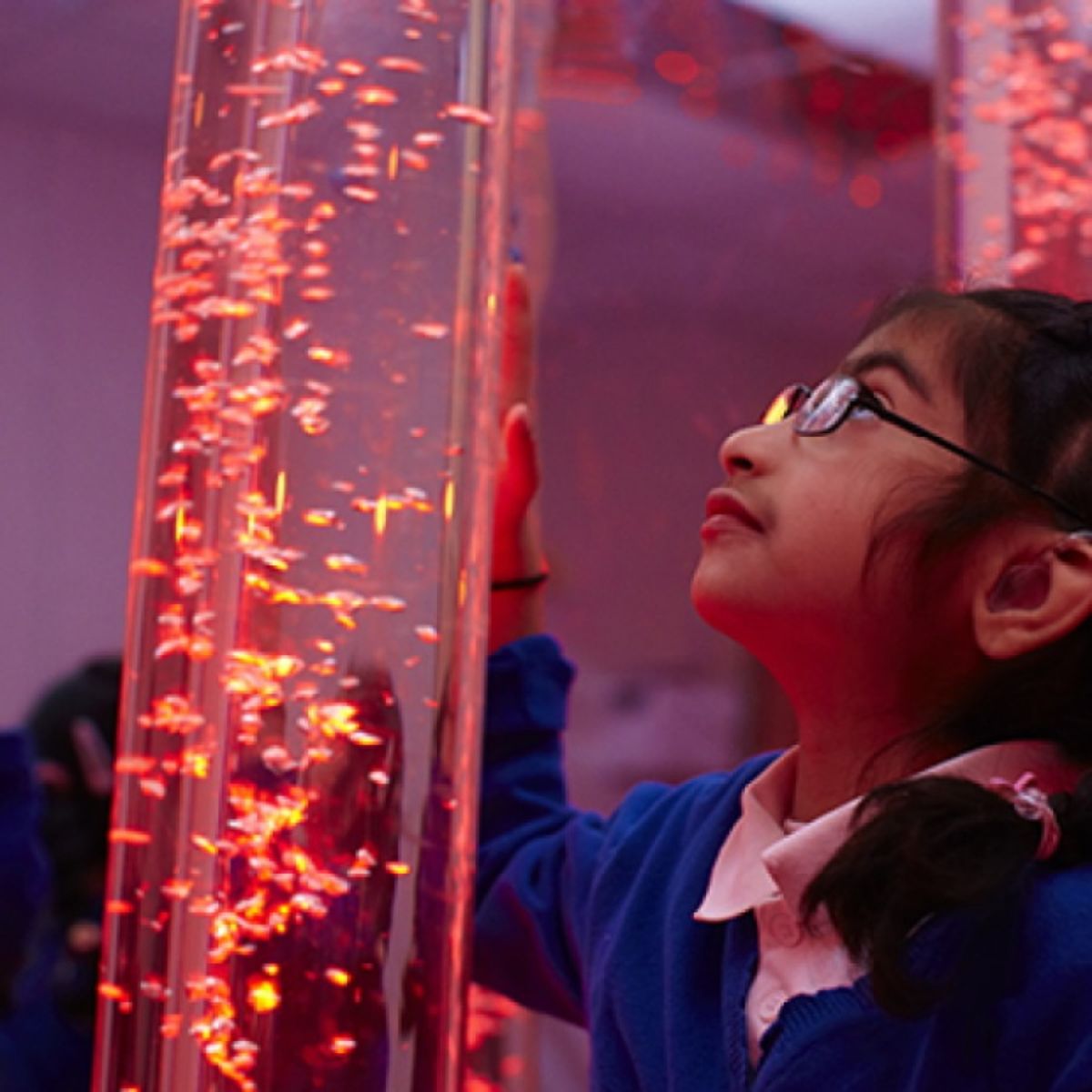 Child with hand on Calming LED Sensory Bubble Tube and staring at the fish inside it 