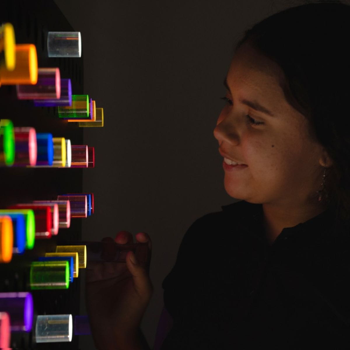 Closeup of girl looking at the PixelPop Interactive Sensory Light Wall Panel in the dark and the pegs lit up