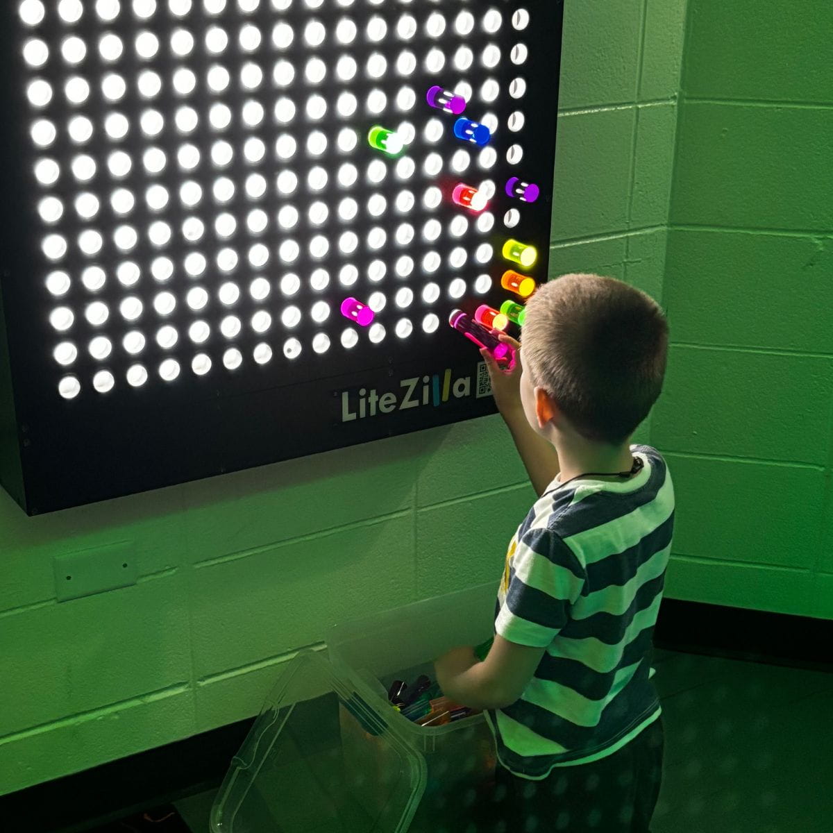 Kid placing a LitePin in the LiteZilla Lite Brite Wall creating a design