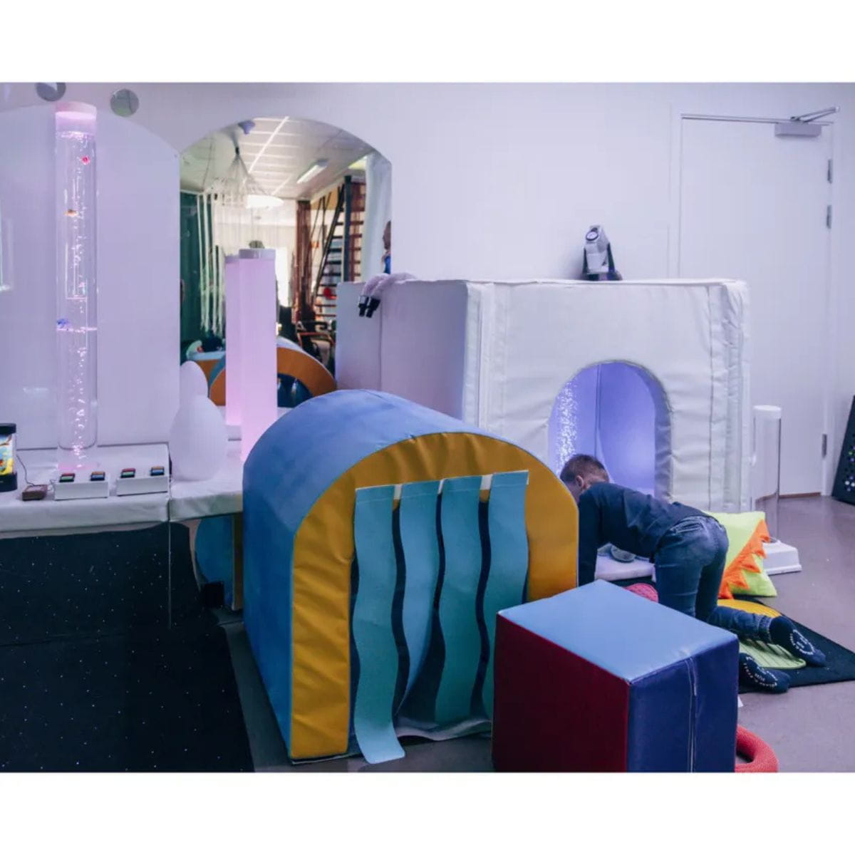 Kid crawling in the Portable Sensory Den with other sensory toys around the room