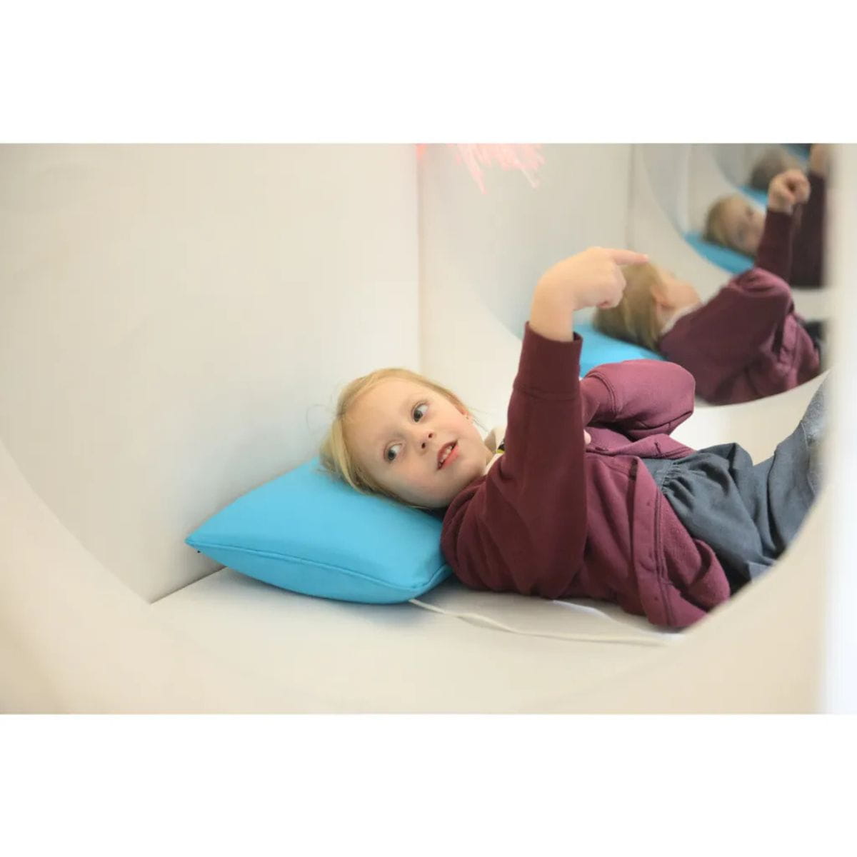Kid laying on pillow inside the sensory den tent with her reflection in the mirror