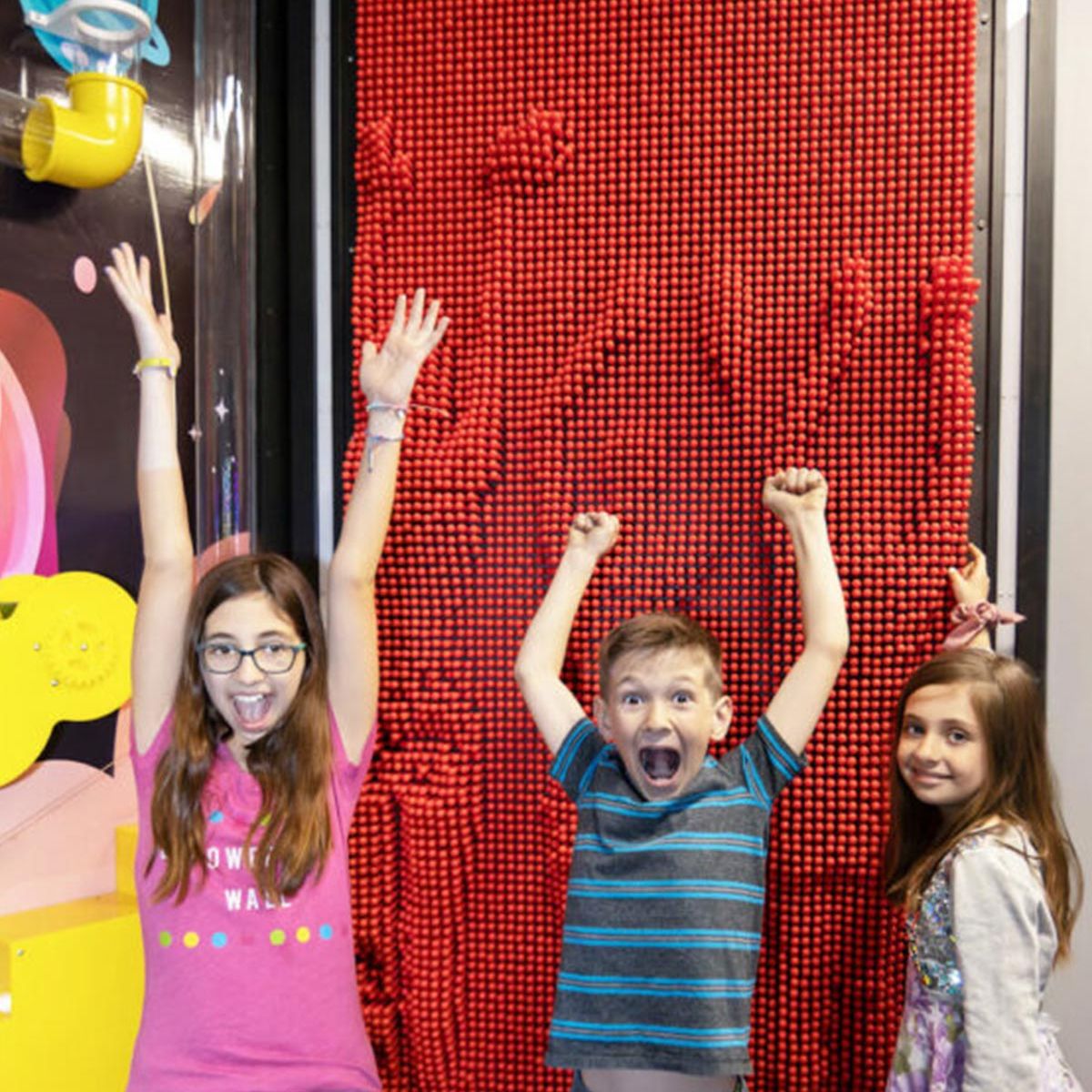 Three kids with excitement on their faces standing in front of the Clone Box Giant Pin Wall